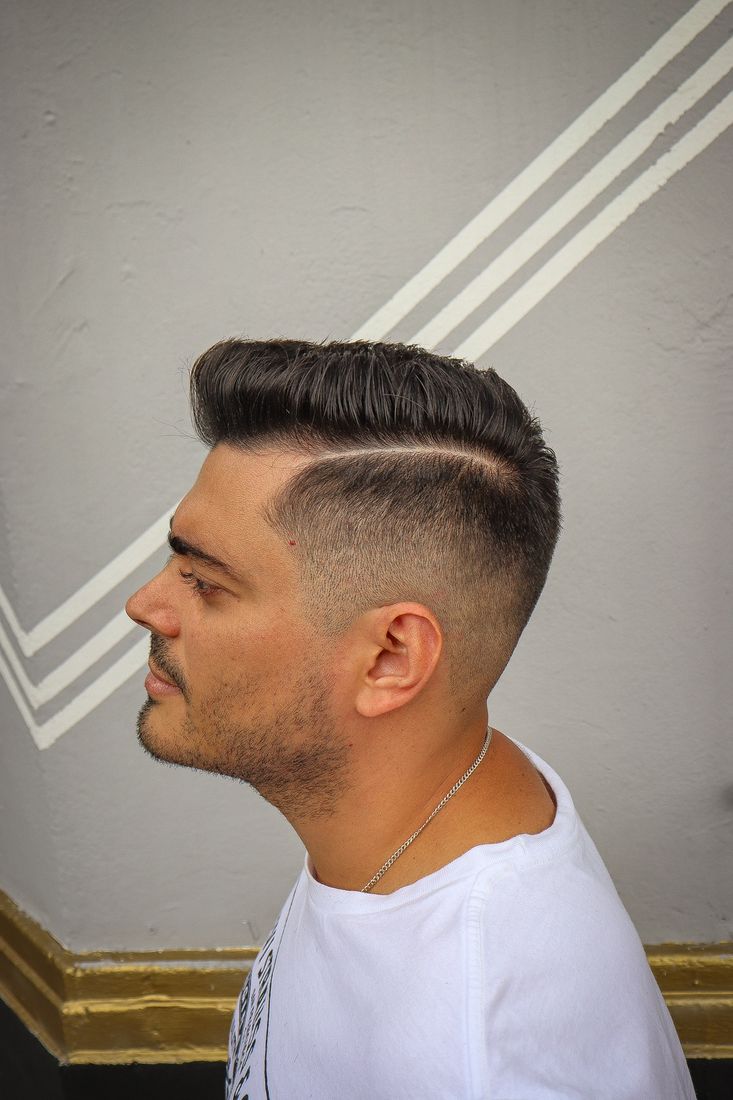 Corte pompadour con desvanecido lateral y raya marcada, visto de perfil.