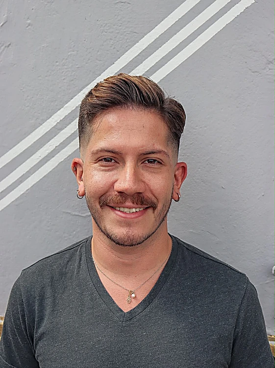 Cliente sonriendo con un corte texturizado recién hecho, frente al muro rayado.